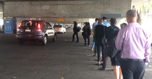 People lined up under a freeway overpass waiting to get in cars to commute across the SF Bay Bridge, "casual carpool" style.